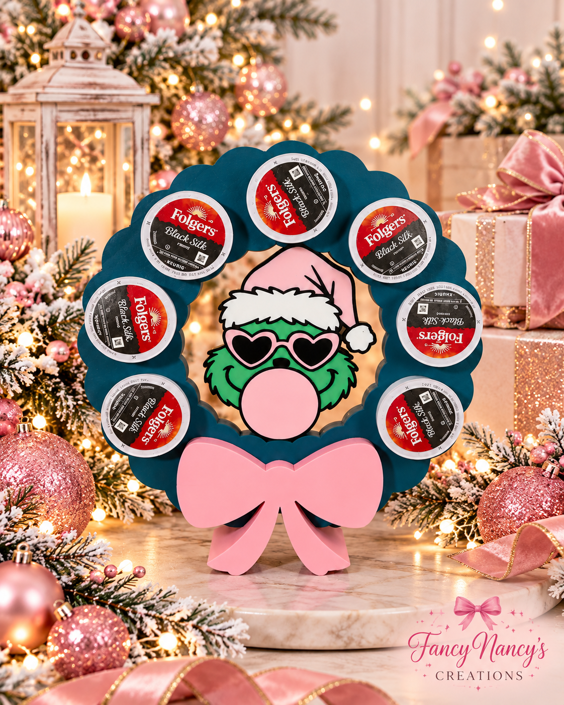 Teal Grinch wreath coffee pod holder displaying seven pods, with a pink bow and green character wearing a pink Santa hat and heart-shaped glasses.